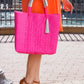 Woman wearing orange dress and brown heels holding a hot pink woven bucket bag in a city setting