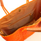 Inside tan lining featuring zipper pocket and magnetic closure of side angle of orange woven tote bag made from recycled plastics