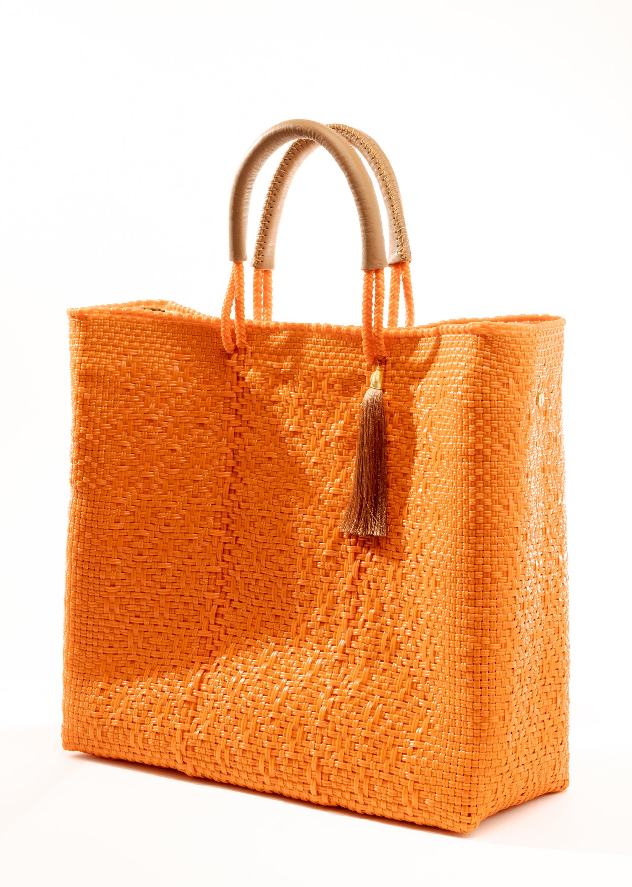 Side angle of orange woven tote bag made from recycled plastics with tan handles and tan tassel detail